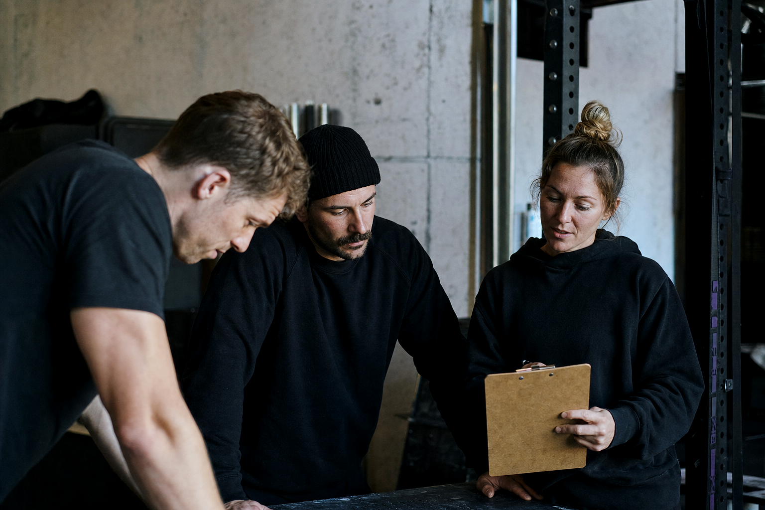 IRONROOT Athletic Club team at work — CANDID GROUP SHOT of three people interacting in a workspace, warm office light, real moment